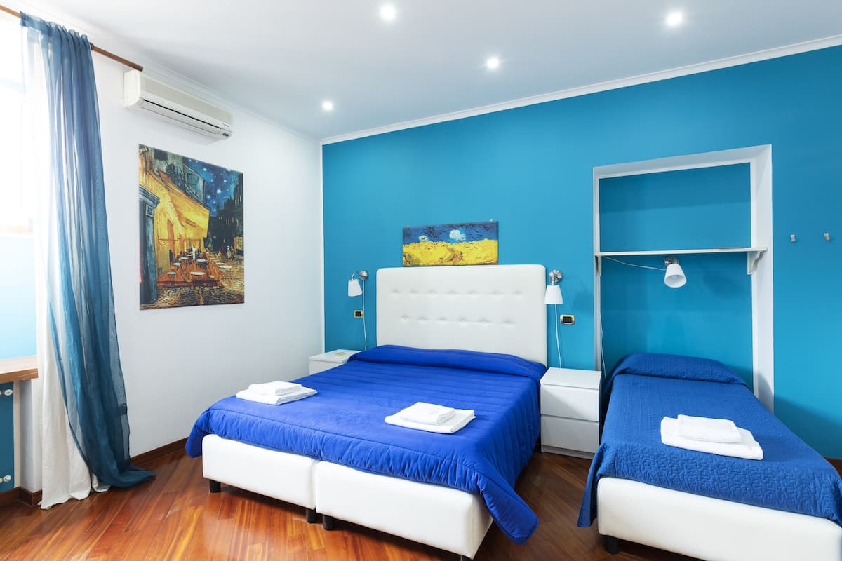 A hotel room with a large bed, a smaller bed, and a window with blue curtains.