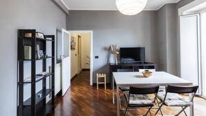 Un espace repas moderne avec une table blanche, des chaises noires et un téléviseur posé sur un meuble noir.