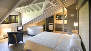 A bedroom with a large bed, a desk with a computer, a bathtub, and a walk-in closet. - La Posada de Langre (Ribamontan al Mar)