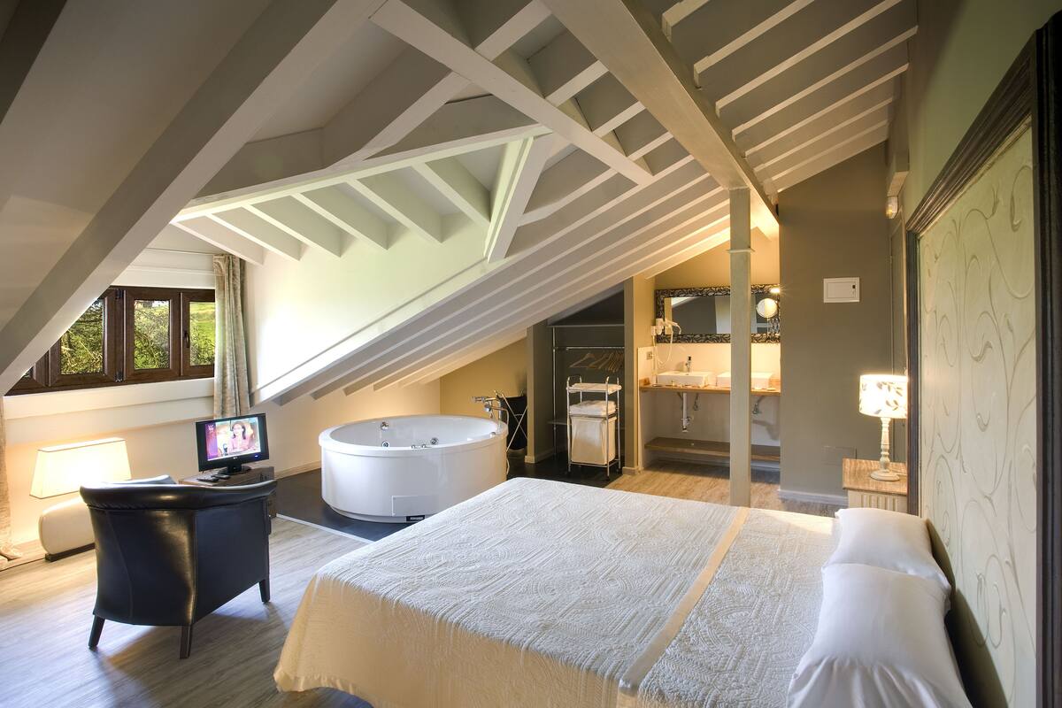A bedroom with a large bed, a desk with a computer, a bathtub, and a walk-in closet.