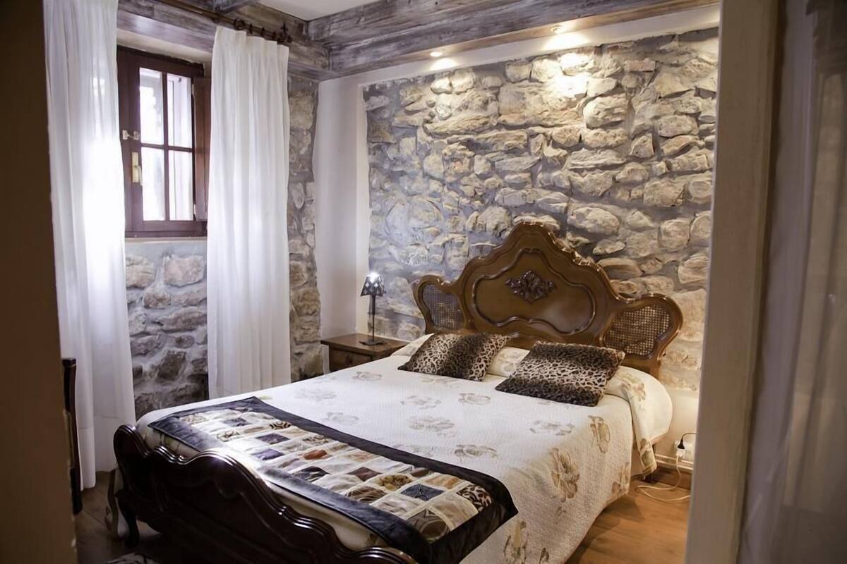 A bedroom with a stone wall, a wooden bed frame, and a quilted bedspread.