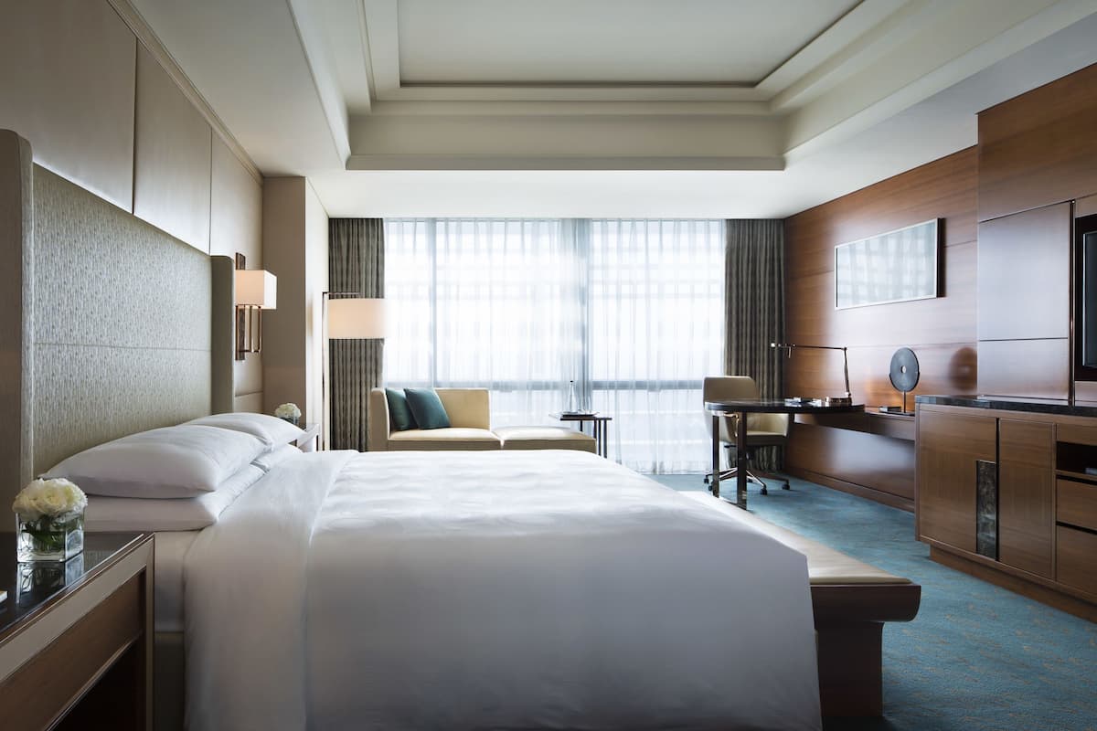 Une chambre d’hôtel avec un grand lit, un bureau avec une chaise, une télévision et une fenêtre avec des rideaux.