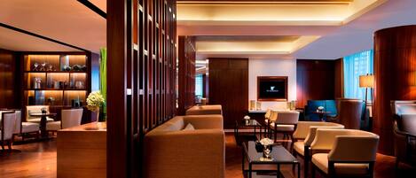 A modern hotel lobby with a wooden reception desk, comfortable seating, a TV, and a well-lit ambiance.