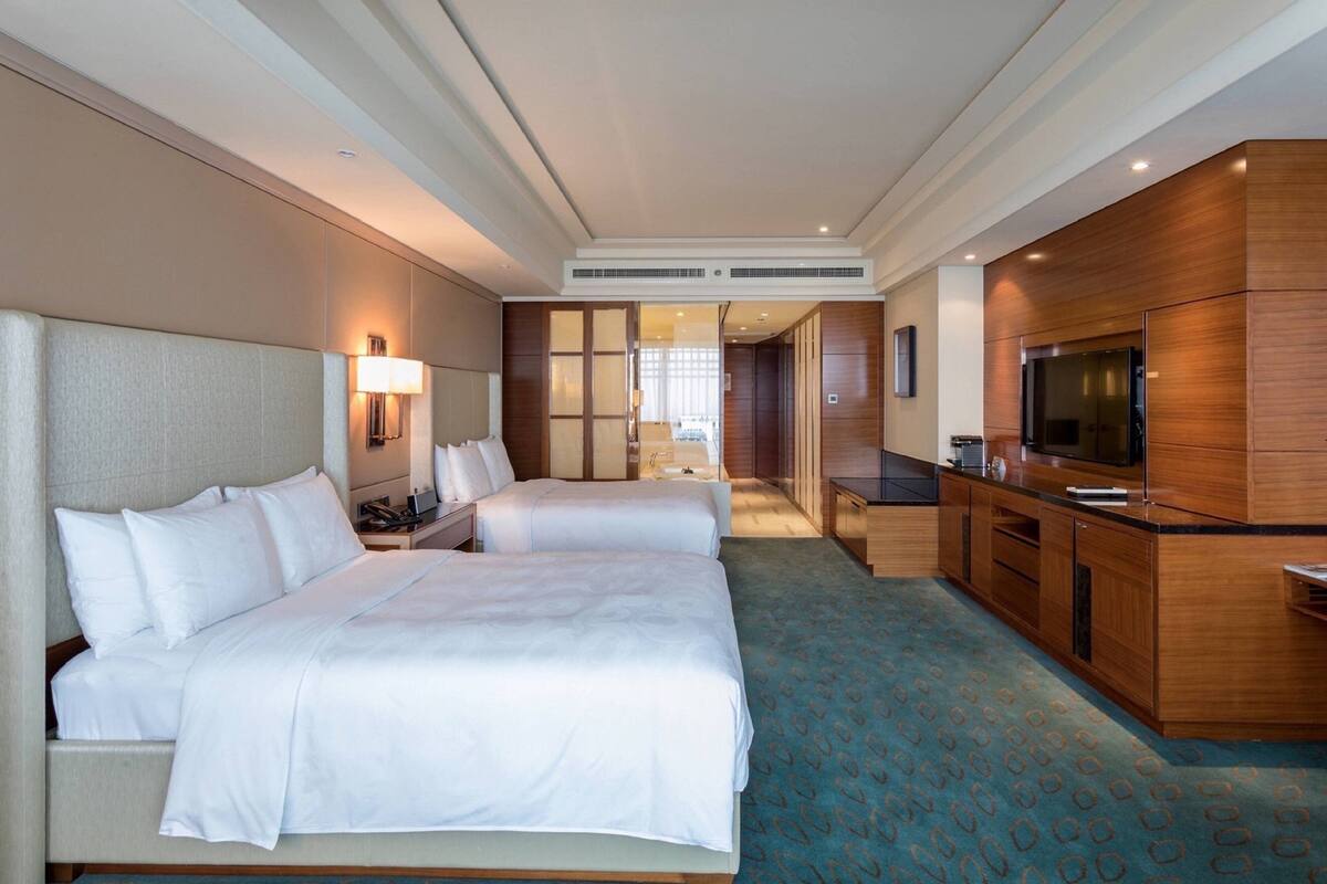 Une chambre d’hôtel avec deux lits, une kitchenette, une télévision et une salle de bain visible à travers une porte en verre.