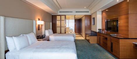 A hotel room with two beds, a kitchenette, a TV, and a bathroom visible through a glass door.