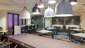 A modern hotel dining area with multiple tables and chairs, pendant lighting, and a view of the city through large windows. - Fairfield Inn & Suites Springfield Northampton/Amherst (Northampton)