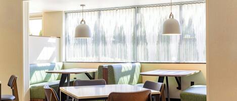 Une chambre d’hôtel dotée d’un coin repas avec des tables et des chaises, d’une grande fenêtre avec des rideaux et d’une vue sur la verdure environnante.