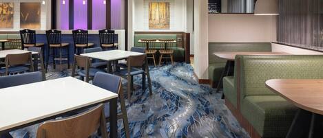 A restaurant with booths and tables, a patterned carpet, and pendant lighting.
