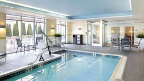 An indoor swimming pool with clear glass walls, a poolside seating area, and a reception desk. - Fairfield Inn & Suites Springfield Northampton/Amherst (Northampton)