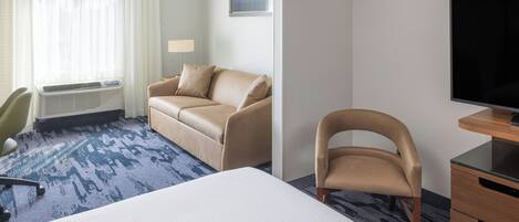 A hotel room with a bed, a sofa, a chair, a TV, and a desk.
