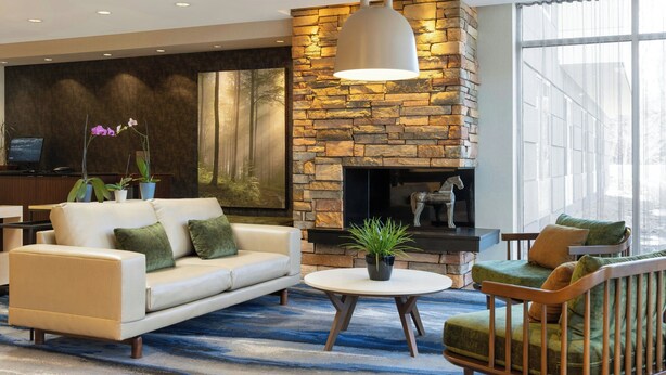 A modern living room with a stone fireplace, a white sofa, a round coffee table, and a green armchair. - Fairfield Inn & Suites Springfield Northampton/Amherst (Northampton)
