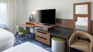 A hotel room with a bed, a desk with a flat-screen TV, a green office chair, a wooden cabinet, and a large mirror.