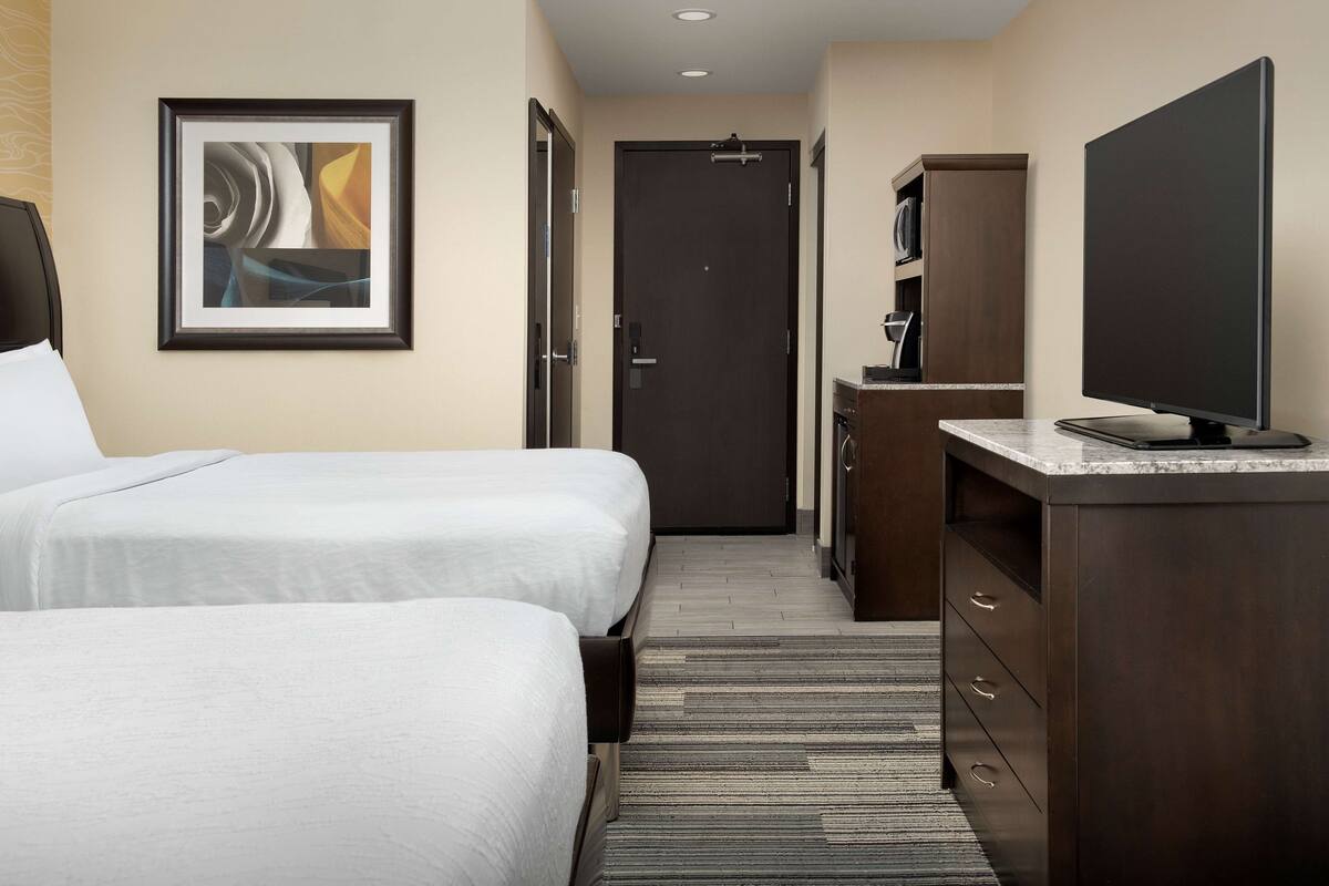 A hotel room with two beds, a TV, a desk, and a door leading to a bathroom.