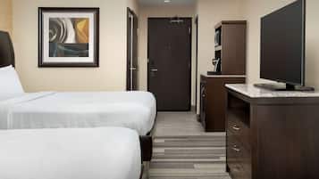 Une chambre d’hôtel avec deux lits, une télévision, un bureau et une porte donnant sur une salle de bain.