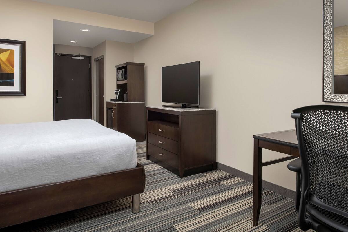 A hotel room with a bed, a desk, a television, a wardrobe, and a chair.