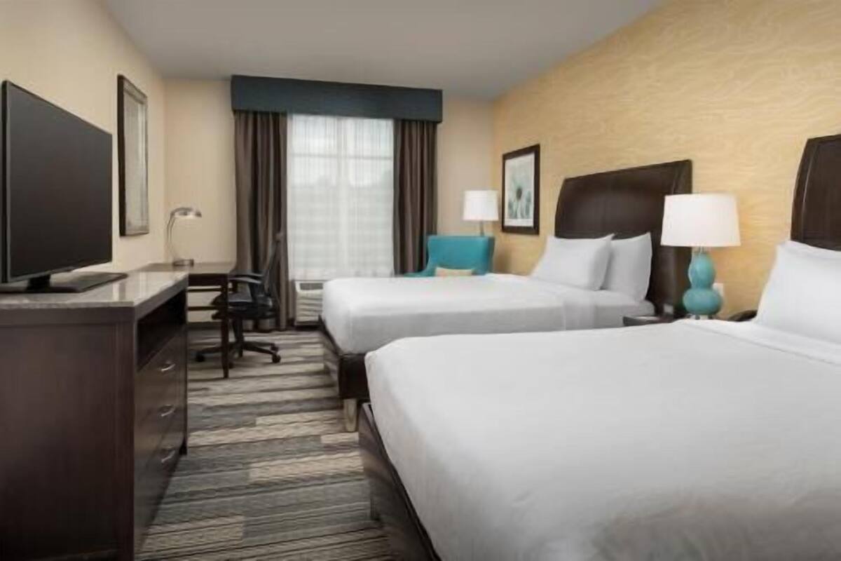 A hotel room with two beds, a desk, a TV, and a window with curtains.