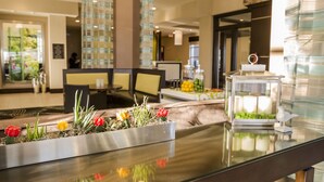 A reception area with a glass-top table displaying a flower arrangement and a candle holder. - Hilton Garden Inn Murfreesboro (Murfreesboro)