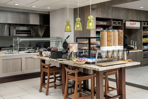 A modern kitchen area with a central island, bar stools, a waffle maker, and a coffee station.