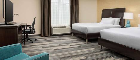A hotel room with two beds, a desk with a computer, a chair, and a TV.