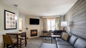 A hotel room with a fireplace, a flat-screen TV, a sofa, a desk, and a chair. - Residence Inn Bloomington (Bloomington)