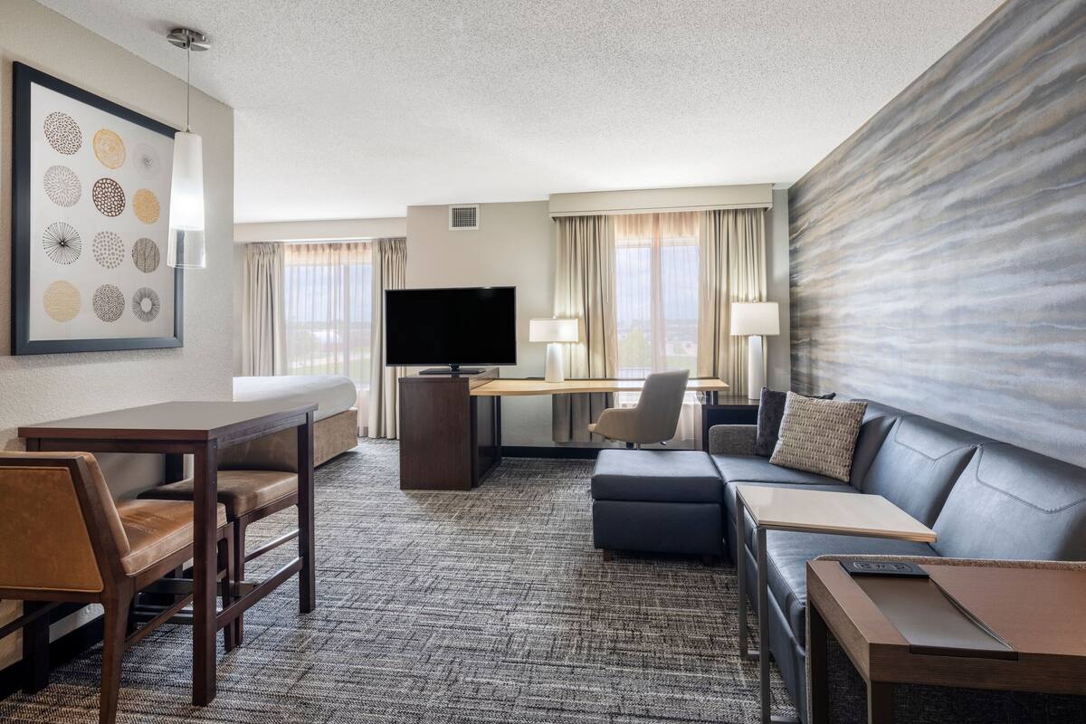 A hotel room with a flat-screen TV, a sofa, a desk with a chair, and a dining table with chairs.