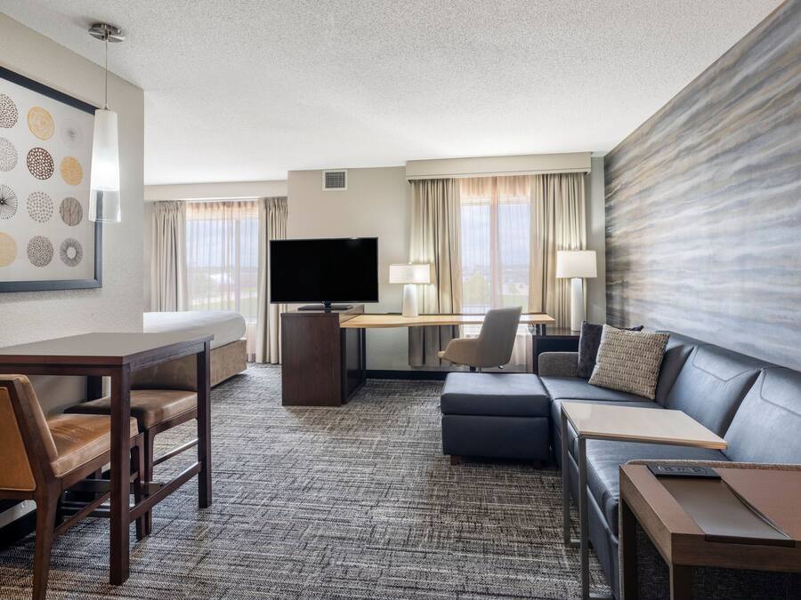 A hotel room with a flat-screen TV, a sofa, a desk with a chair, and a dining table with chairs.