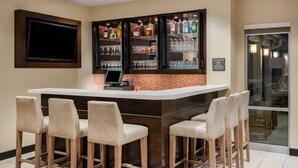 A bar area with a flat-screen TV, multiple shelves of liquor bottles, and bar stools. - Residence Inn Bloomington (Bloomington)