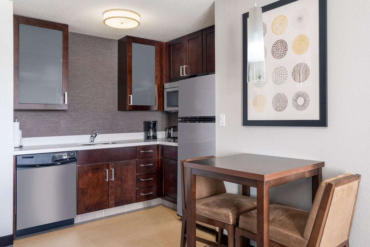 A modern kitchen with dark wooden cabinets, stainless steel appliances, and a dining area with a wooden table and chairs.