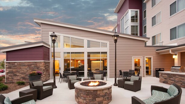 A patio area with outdoor seating, a fire pit, and a building with large windows and a stone wall. - Residence Inn Bloomington (Bloomington)