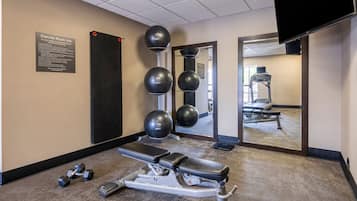 Une salle de sport équipée d’un banc, d’haltères et de ballons d’exercice.