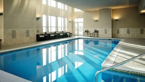 An indoor swimming pool with clear blue water, sunlit walls, and a seating area with chairs and tables. - Residence Inn Bloomington (Bloomington)