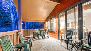 Um deck coberto com área de estar externa e vista para a floresta.