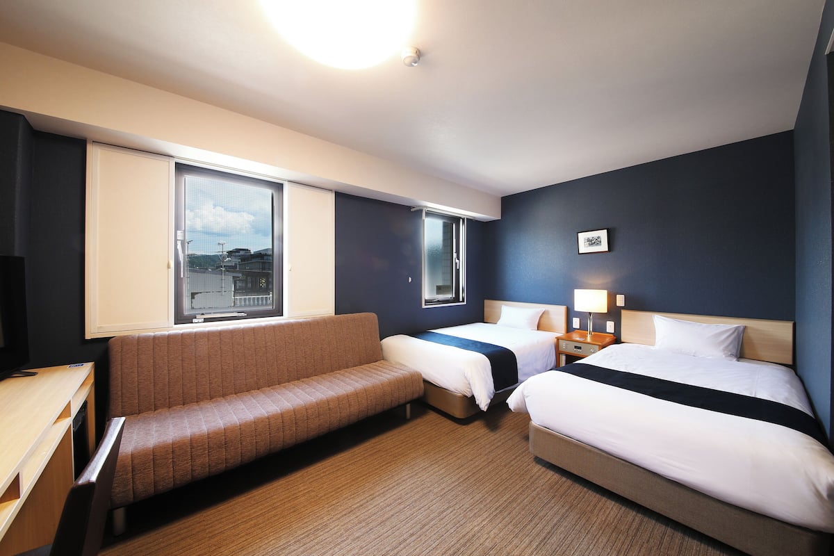 A hotel room with a bed, a sofa, a desk, and a window.