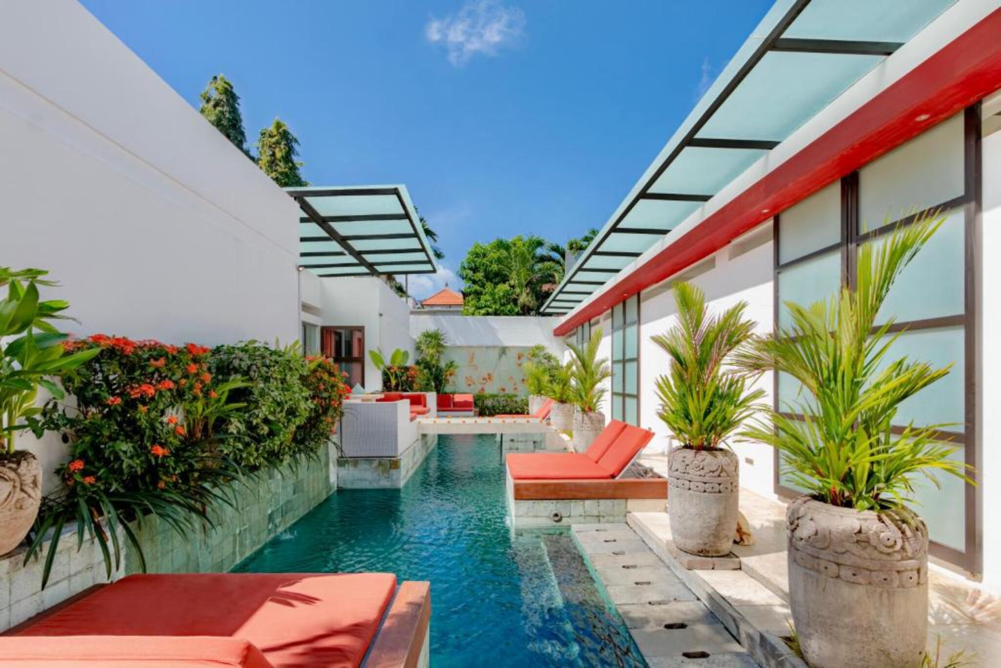 Uma área de piscina moderna com espreguiçadeiras vermelhas, água cristalina e vasos de plantas.