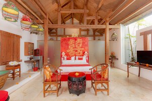 Una camera tradizionale con soffitto in legno, un letto con copripiumino rosso e bianco, un tavolo rotondo con sedie e una televisione su un mobile in legno.