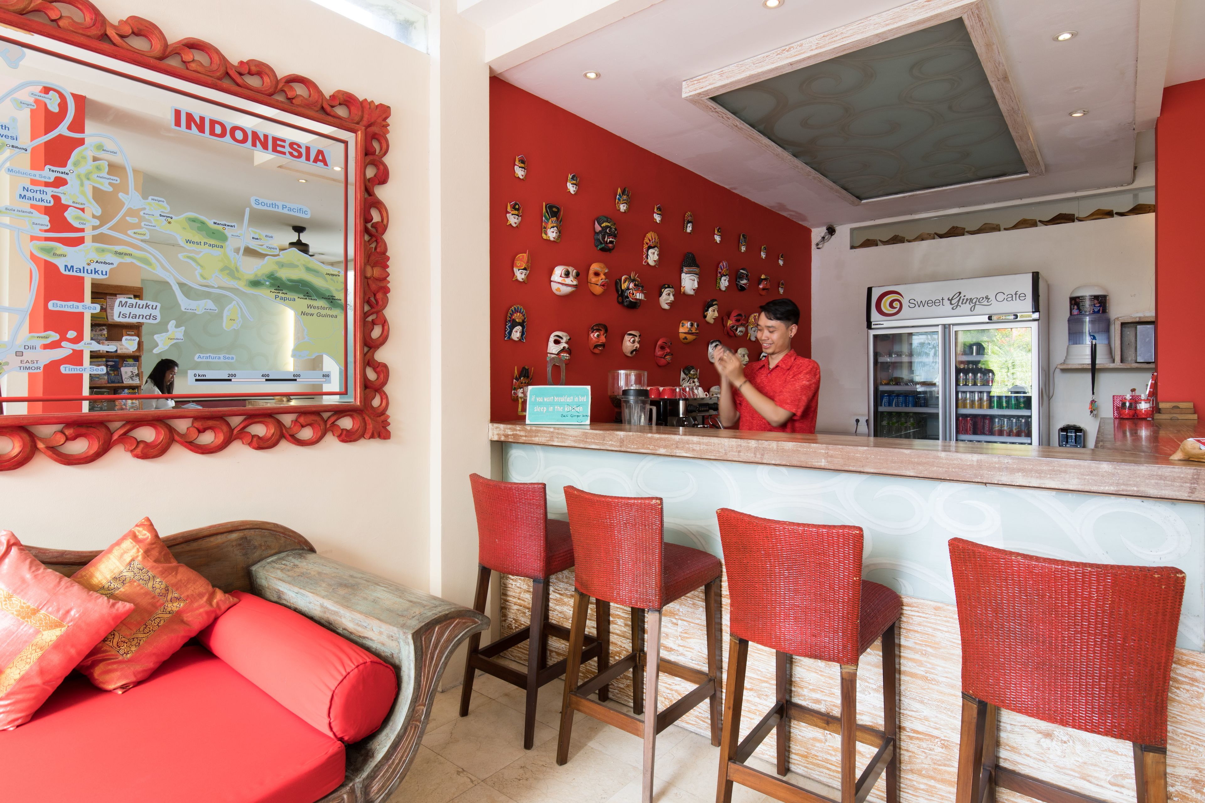 Uma área de bar com parede vermelha, um mapa da Indonésia e uma mulher atrás do balcão.