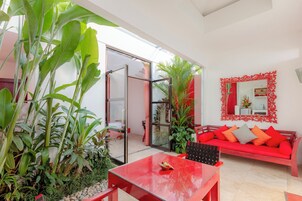 Uma sala de estar moderna com um sofá vermelho, uma porta de vidro que dá para o exterior e um espelho com moldura vermelha na parede.