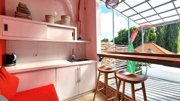Una cocina con armarios blancos, un lavamanos y una ventana con vistas a un balcón desde donde se ve una casa y árboles.