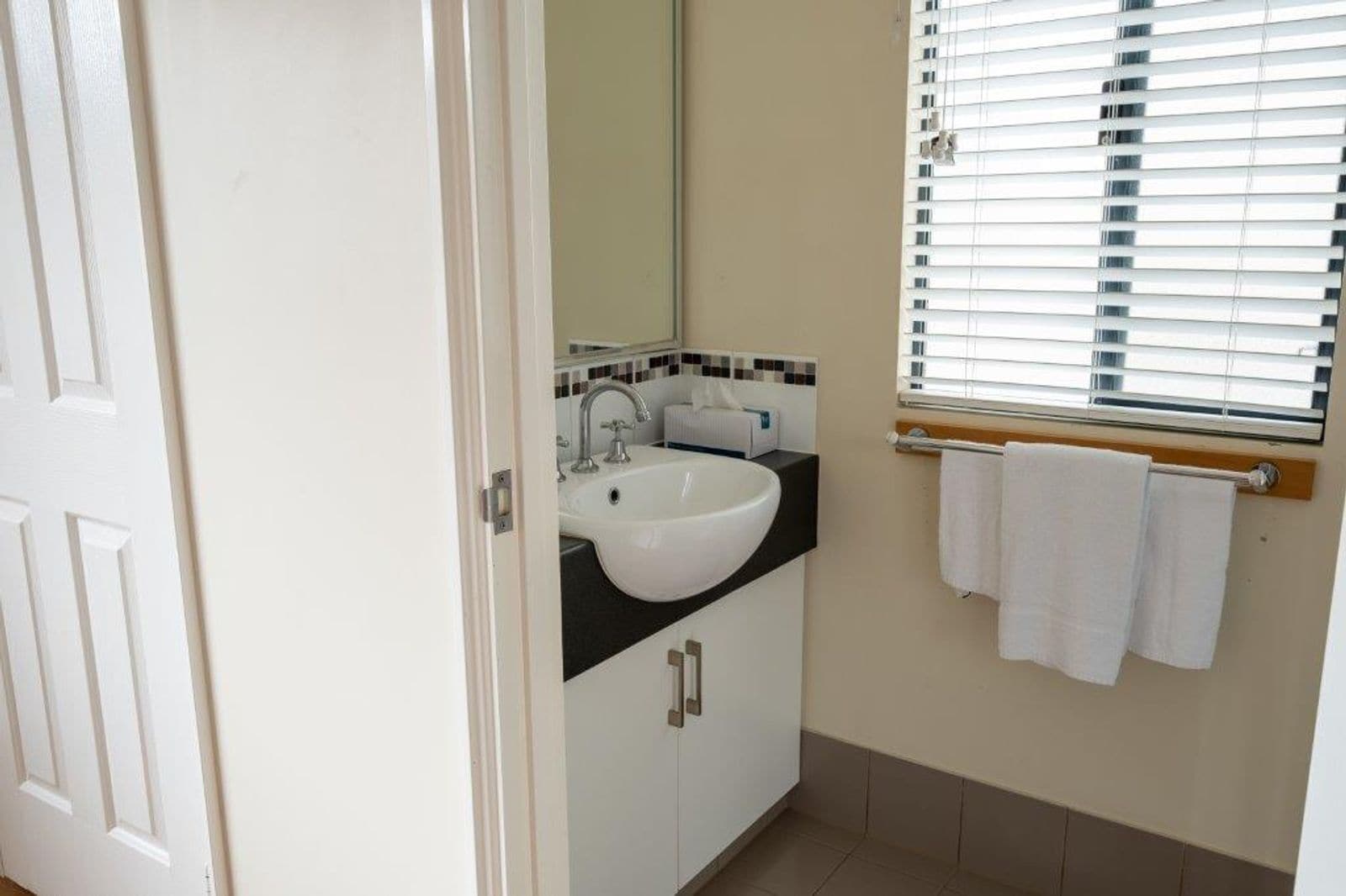 Une salle de bain avec un lavabo blanc, un miroir et une fenêtre avec des stores.