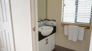 Une salle de bain avec un lavabo blanc, un miroir et une fenêtre avec des stores.