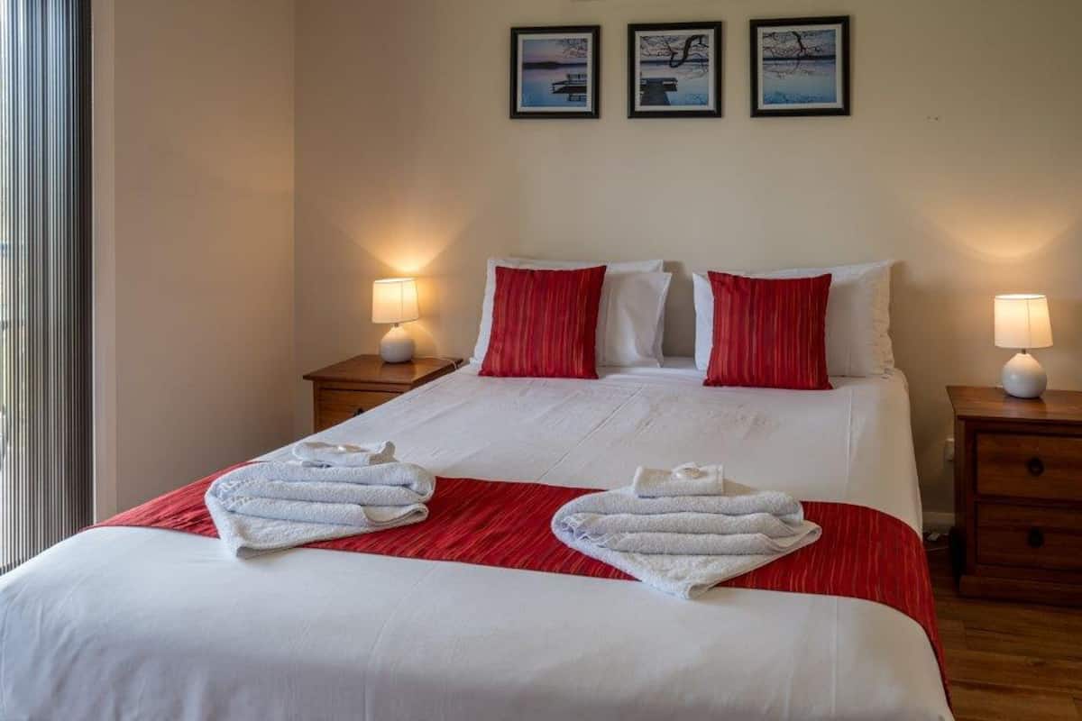 A neatly made bed with white and red bedding, two bedside tables with lamps, and three framed pictures on the wall.