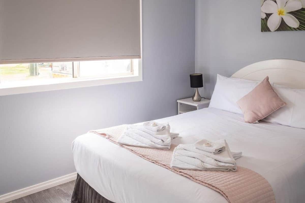 A neatly made bed with folded towels, a bedside lamp, and a window with a view.