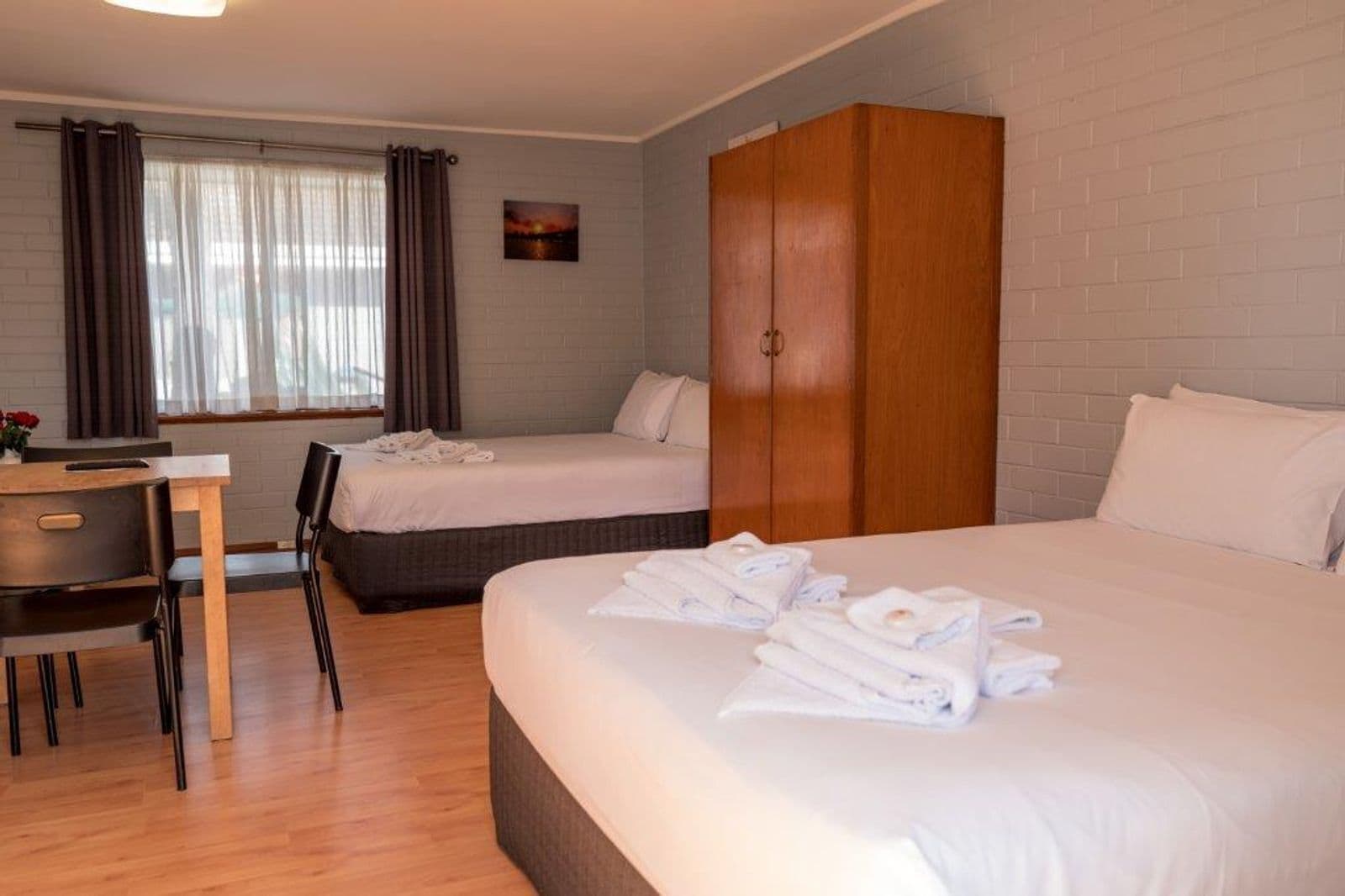 Una habitación de hotel con dos camas, un armario de madera, un escritorio con silla y una ventana con cortinas.