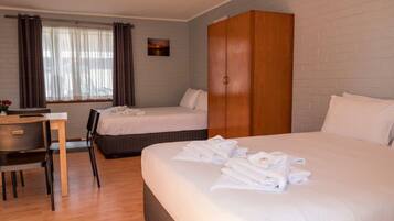 Una habitación de hotel con dos camas, un armario de madera, un escritorio con silla y una ventana con cortinas.