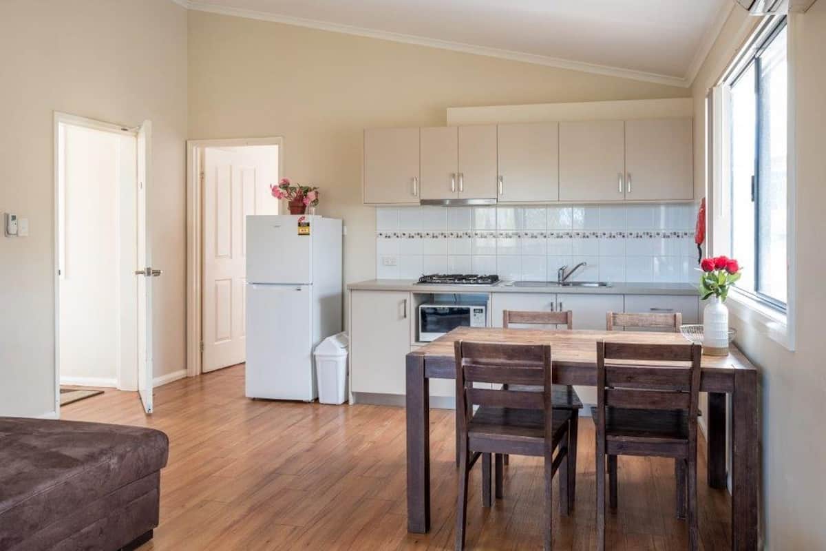 A compact kitchen with white cabinets, a refrigerator, a stove, and a dining area with a wooden table and chairs.