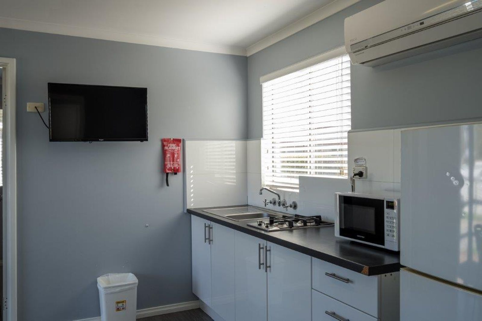 Una cocina con televisión de pantalla plana, microondas, fregadero y manta ignífuga.