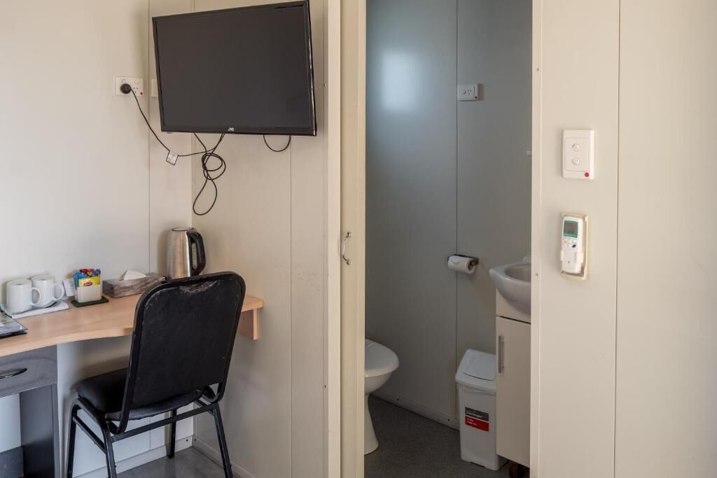 Una habitación pequeña con escritorio, silla, televisor y un inodoro.