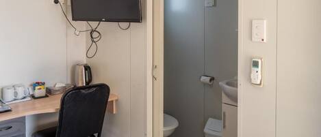 Una habitación pequeña con escritorio, silla, televisor y un inodoro.