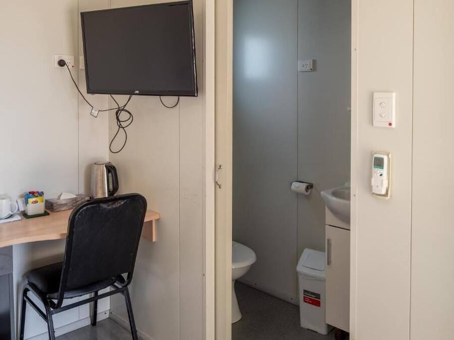 Una habitación pequeña con escritorio, silla, televisor y un inodoro.