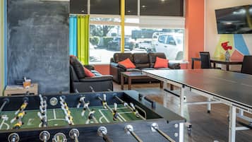 Una habitación con mesa de fútbol, mesa de ping pong, sofá y televisor montado en la pared.